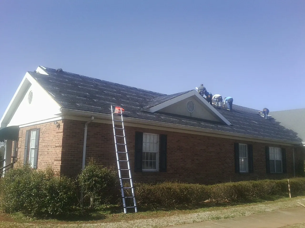 Crew tearing shingles off a brick ranch roof with a ladder set — Metal Roof Repair work by our crew in Onemo
