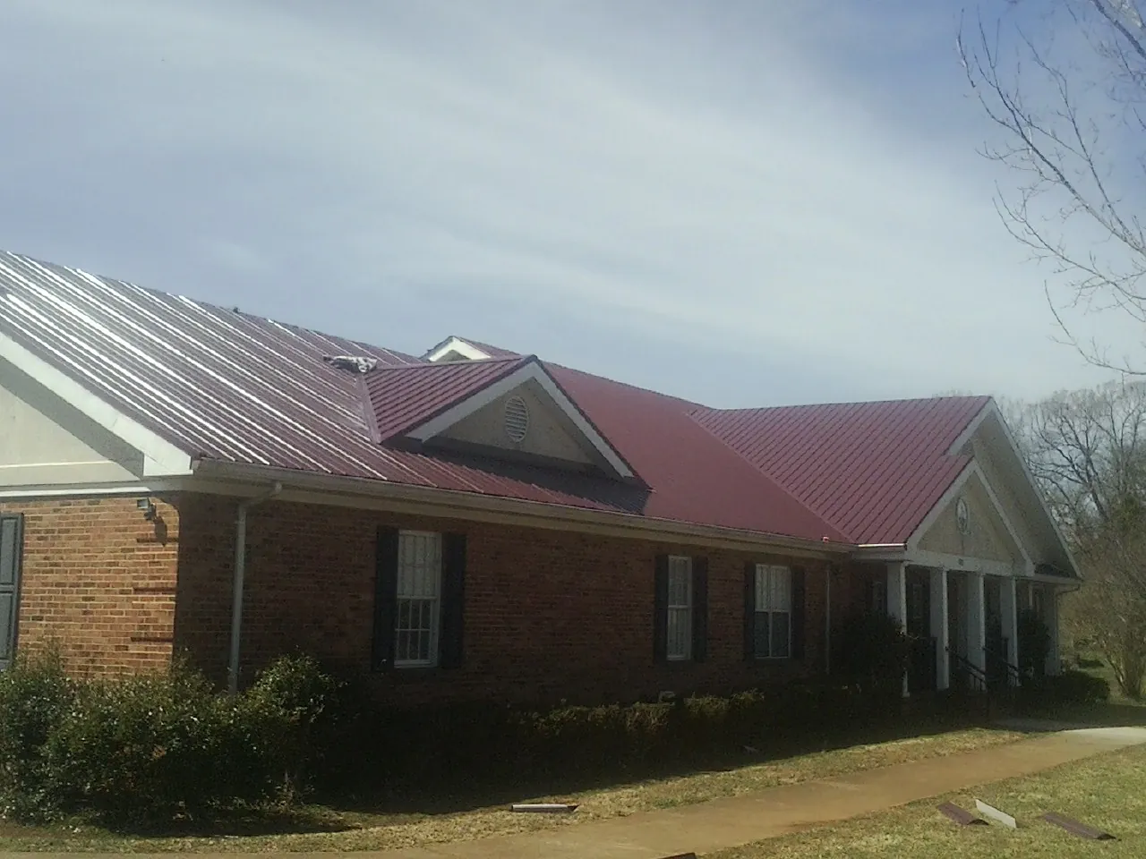 Red metal roof with gabled entries on a long brick building, from a Hail Damage Roof Repair job in Onemo