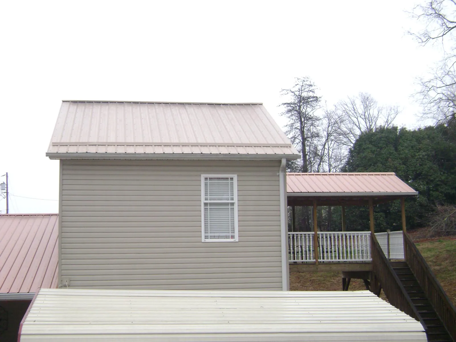 Tan metal roofs on a two story addition and attached porch, from a Roof Replacement job in Onemo